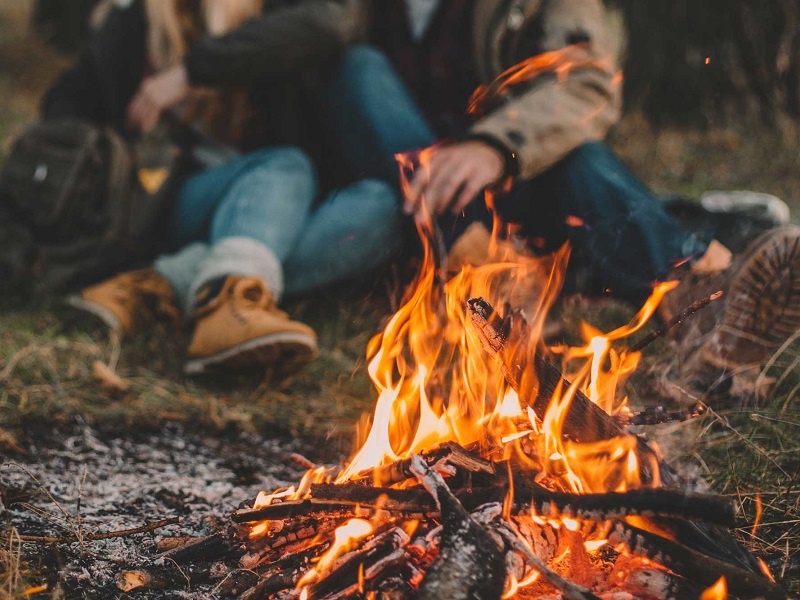 Ein Paar sitzt vor einem Lagerfeuer und will die Asche im Wald entsorgen. 